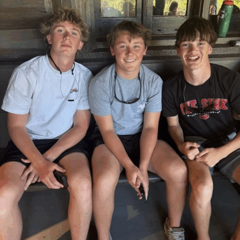 three friends sitting on a bench outside of a log cabin 