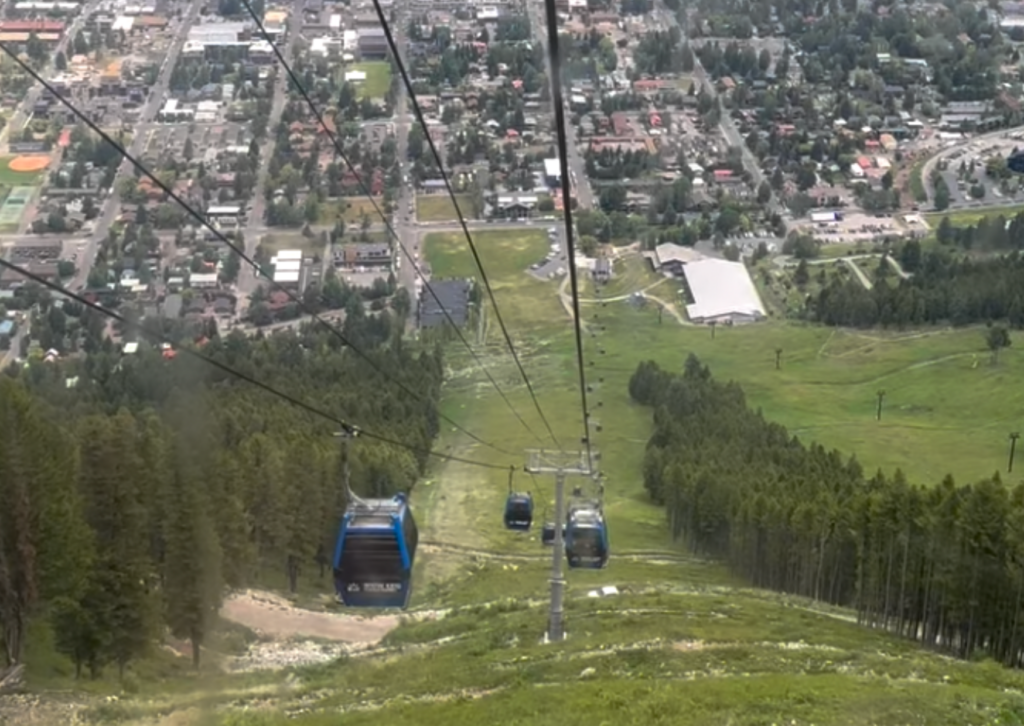 View looking down from the Snow King Mountain gondola, with two blue gondola cabins descending above the town of Jackson, Wyoming