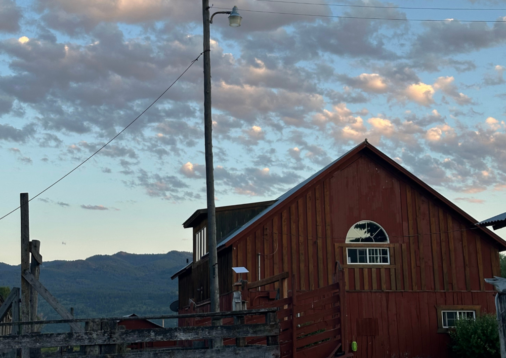 Rustic red ranch barn at dusk with mountains and dramatic cloudy sky in the background