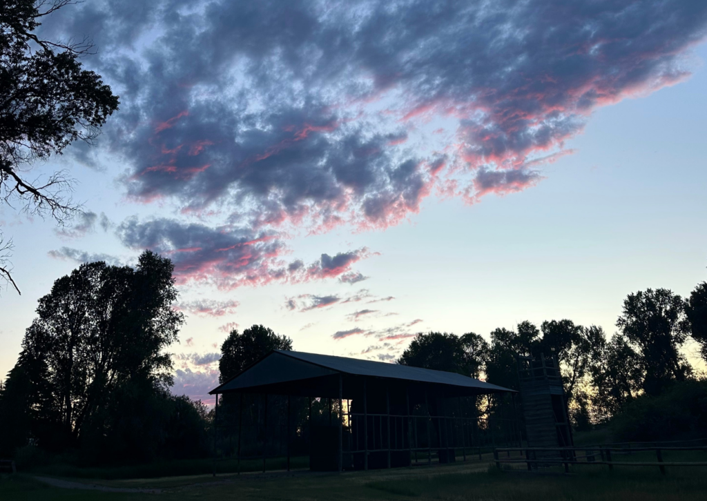 Ranch barn silhouetted against a dramatic pink and blue twilight sky, surrounded by trees