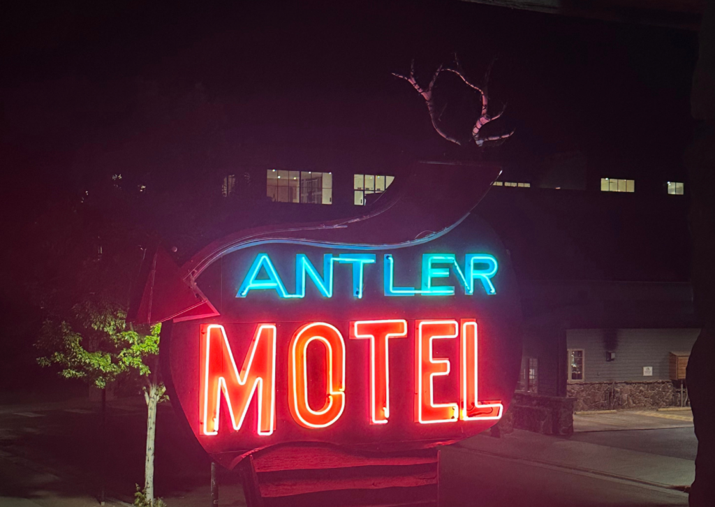 The glowing neon sign for the Antler Motel in Jackson, Wyoming, lit up at night with a moose antler sculpture on top