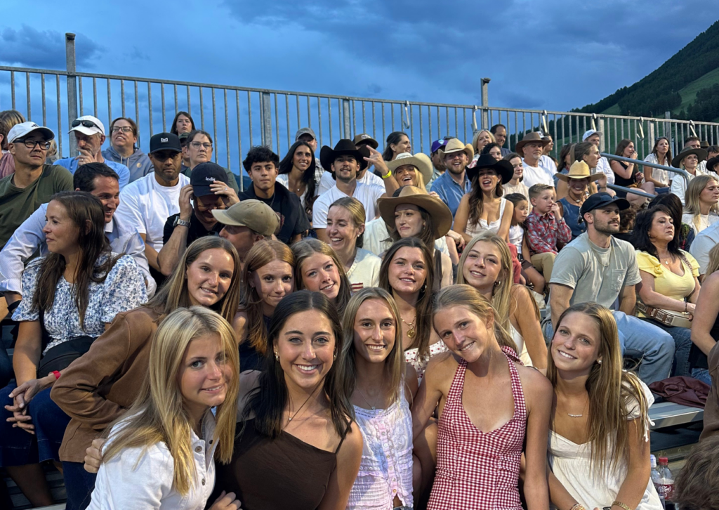 Large group of Grand Western Tour participants seated in the grandstands at the Jackson Hole rodeo, with a mountain visible in the background