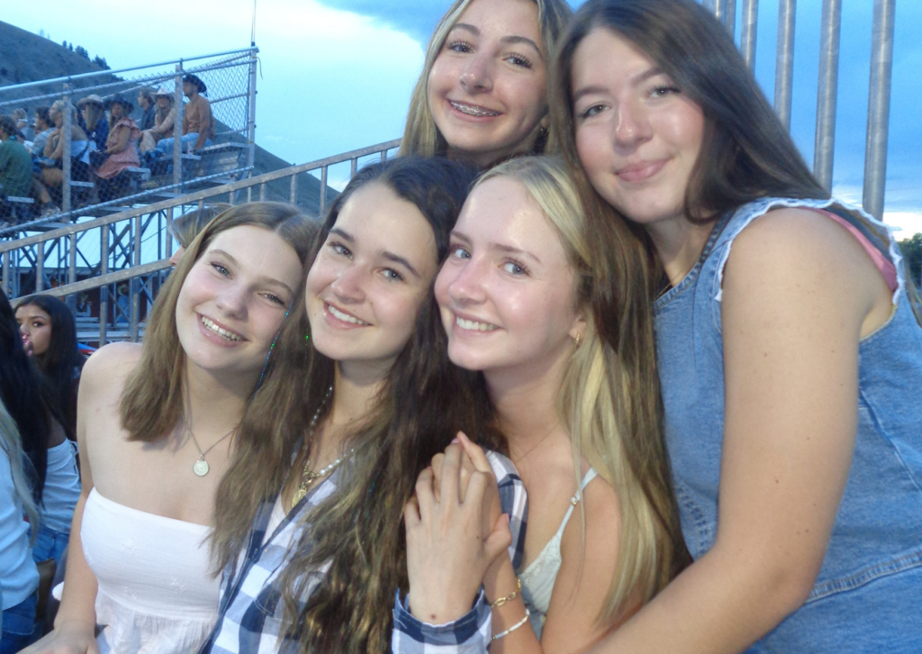 Five teen girls posing together and smiling in the grandstands at the Jackson Hole rodeo