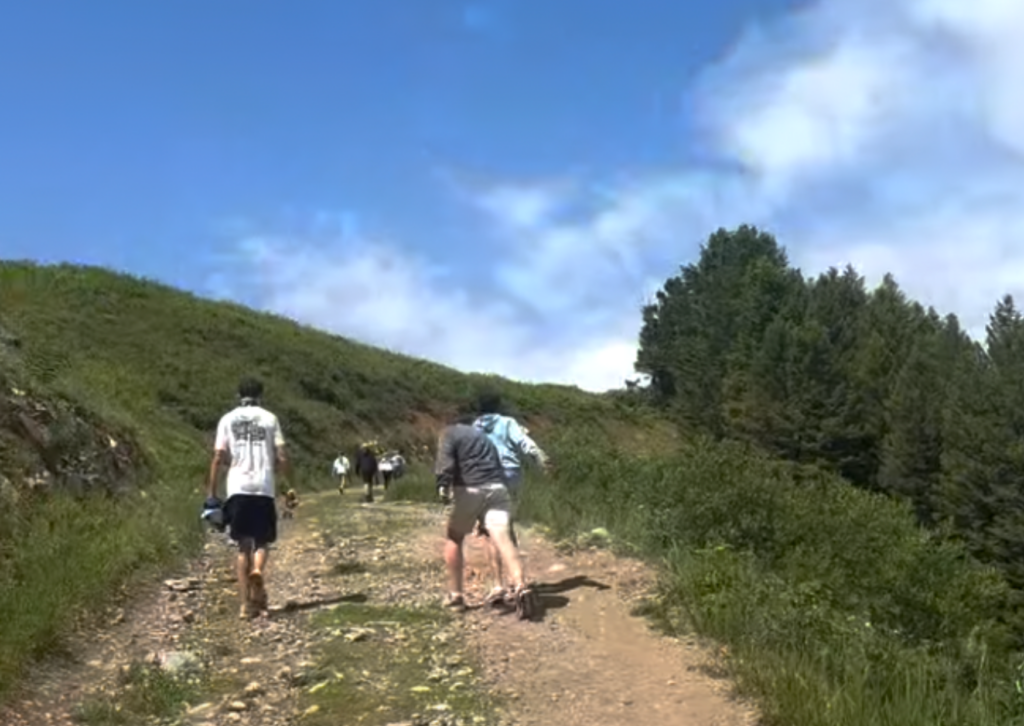Hikers walking up a rocky trail on Snow King Mountain, with green mountain terrain and blue sky above
