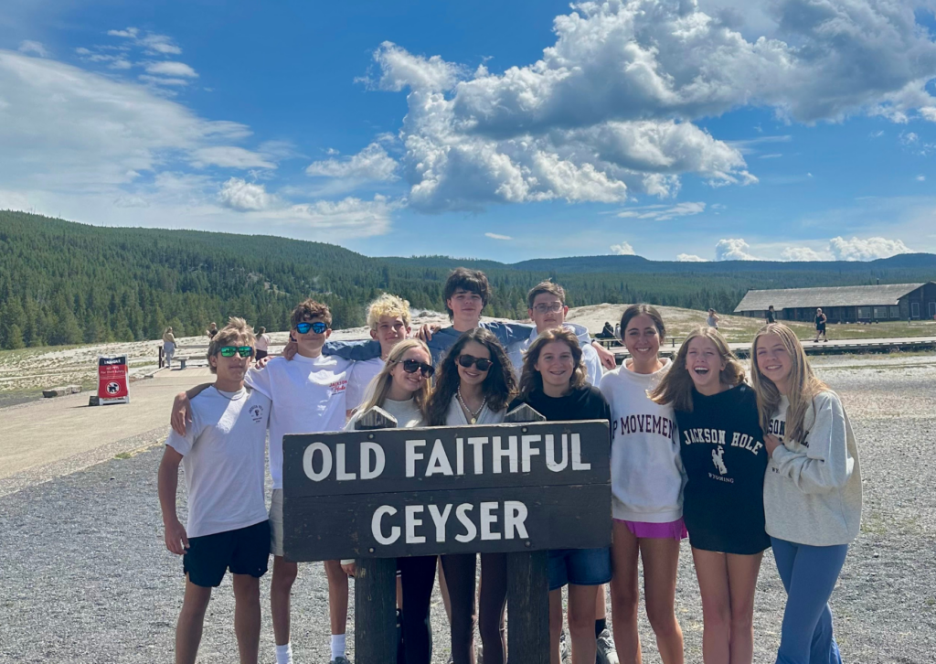 Group of students posing together while holding an Old Faithful Geyser sign at Yellowstone National Park