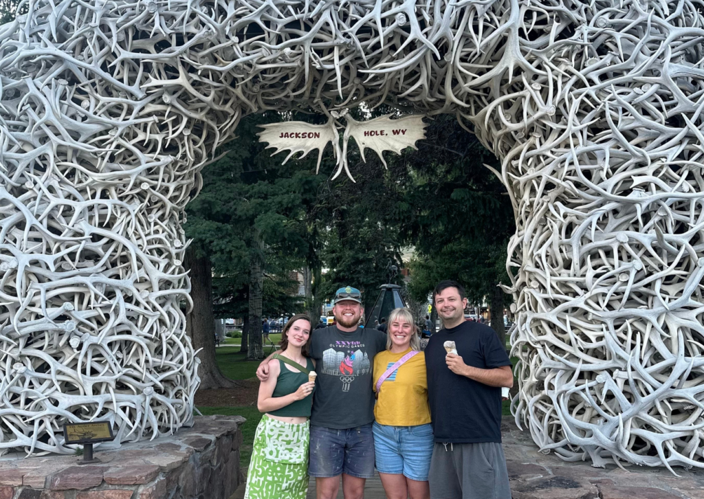 Four Grand Western Tour travelers posing and holding ice cream cones under the iconic antler arch in Jackson Hole, Wyoming