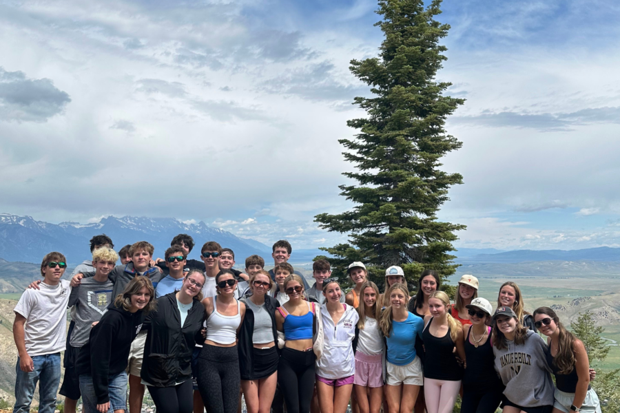 Large group of Grand Western Tour travelers posing together at the summit of Snow King Mountain, with the Teton Range and Jackson Hole valley visible in the background