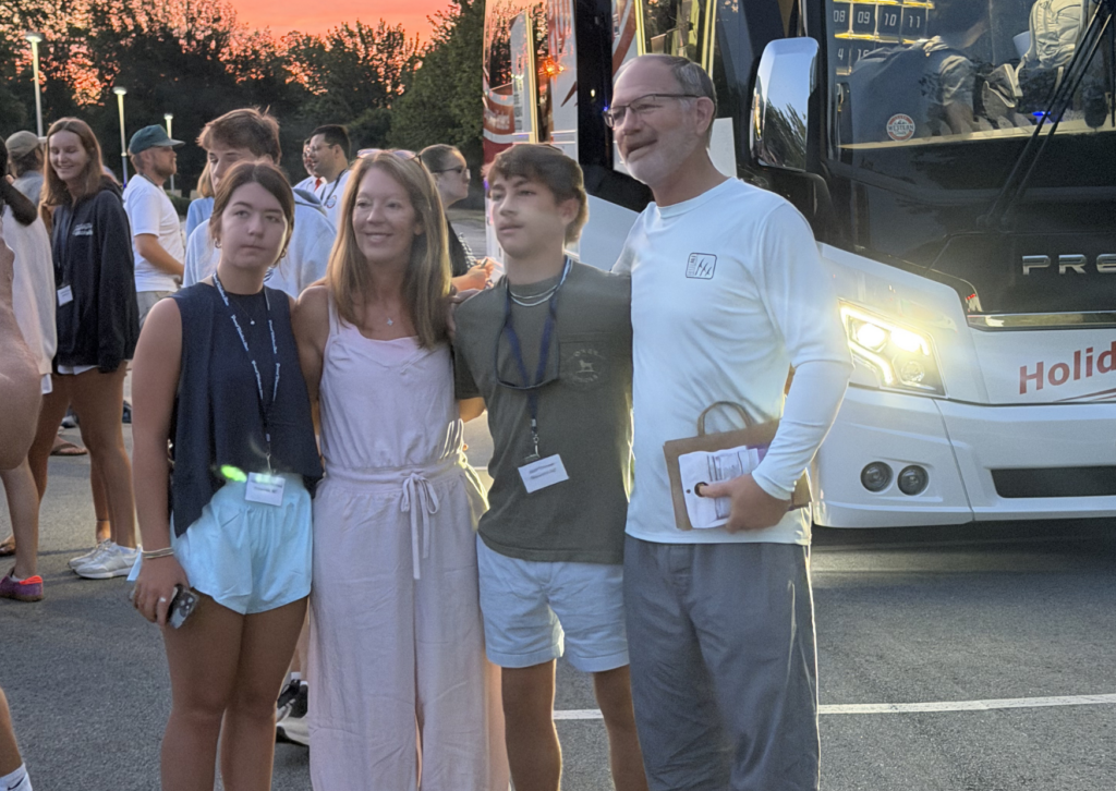 family taking picture in front of tour bus 