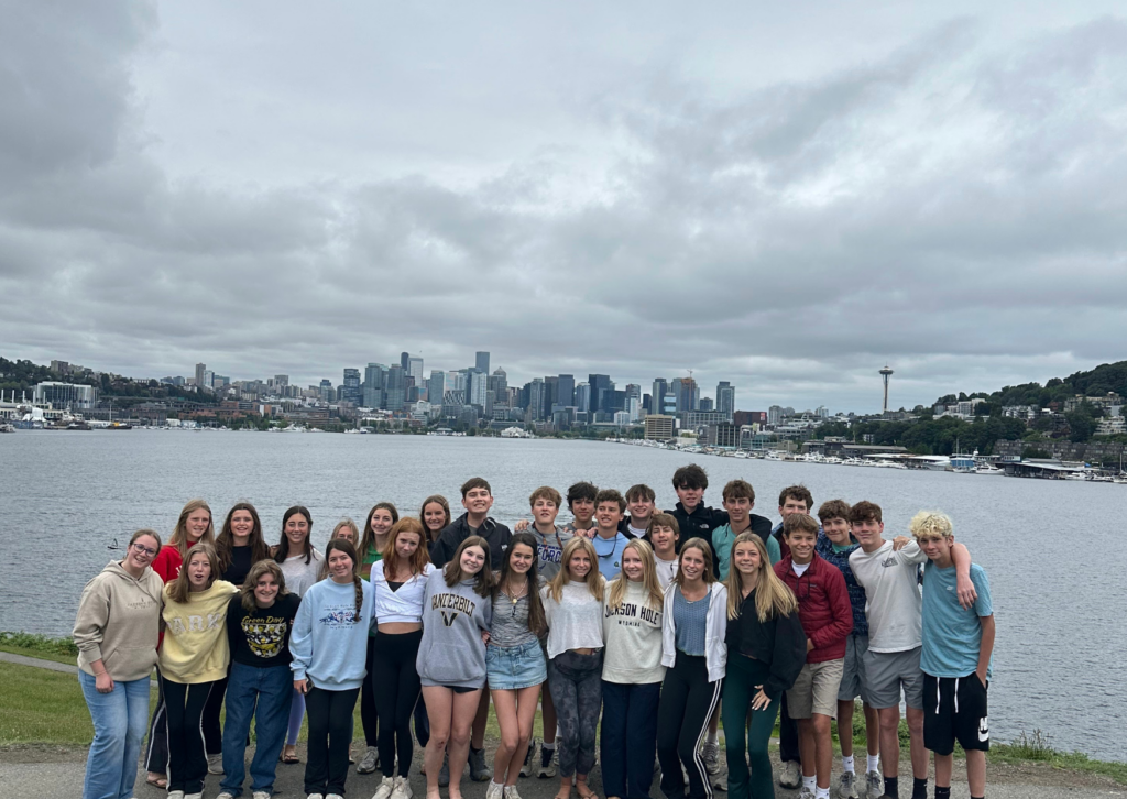 Large group of students posing by the water with the Seattle skyline and Space Needle visible in the background across Lake Union