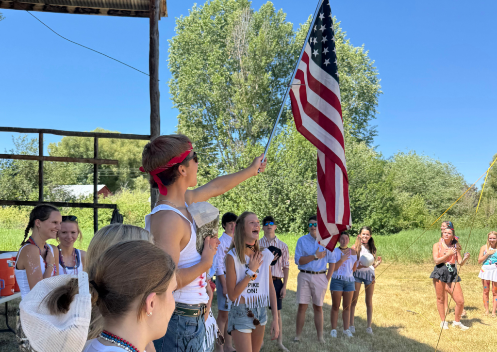students raising an american flag and saying pledge in their costumes