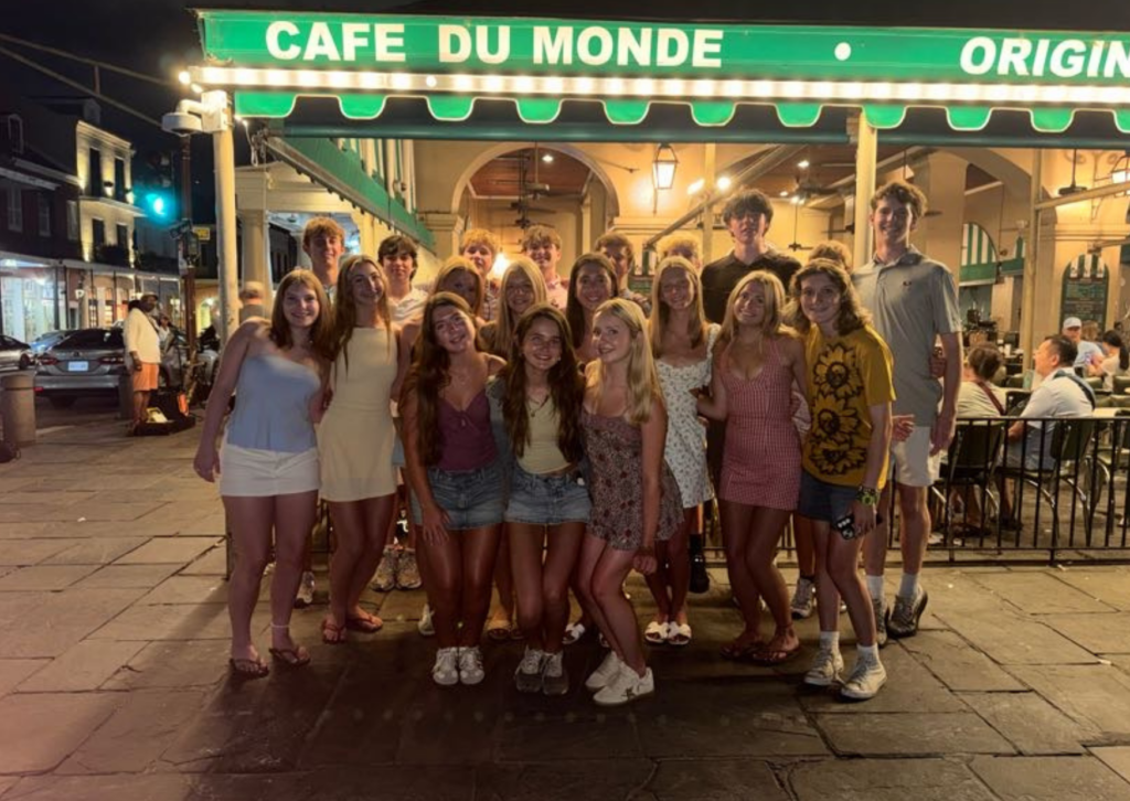Group photo outside Café du Monde at night, with the café's green and white striped awning and string lights in the background.