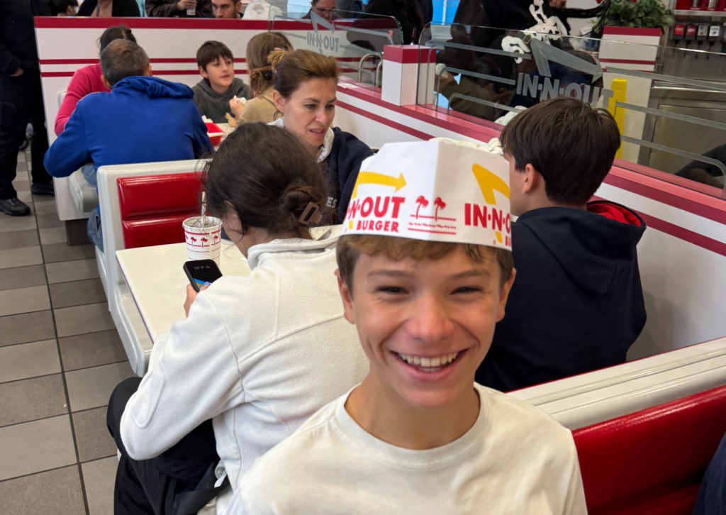 Teenager smiling and wearing a folded paper In-N-Out hat while sitting in a restaurant booth