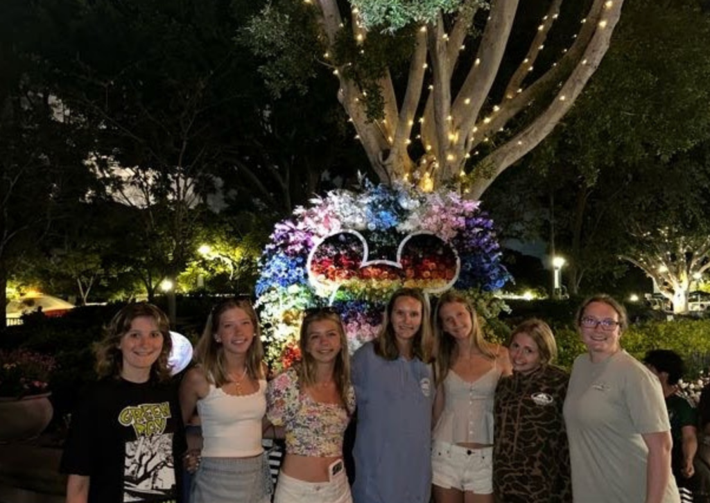 Group of young women posing at night in front of a lit Mickey Mouse floral display at Downtown Disney