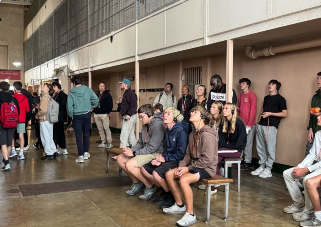 boys sitting on a bench with headphones looking up at museum exhibit