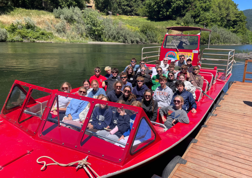 students in a red jet boat on the rogue river facing ahead in oregon