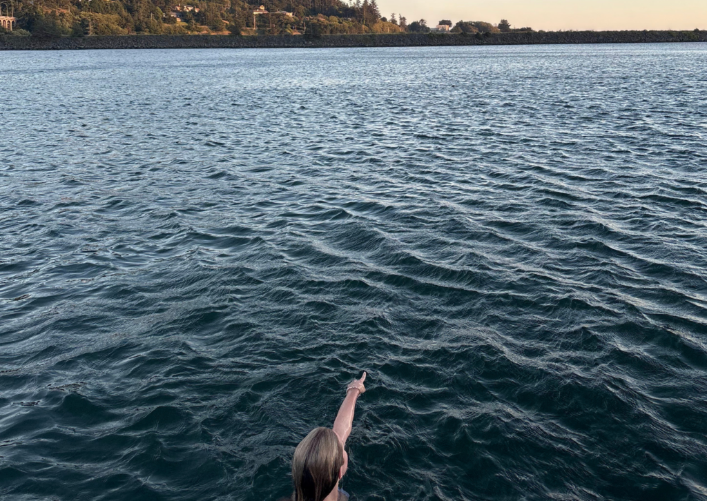 A person pointing out across the calm Rogue River toward tree-lined shores