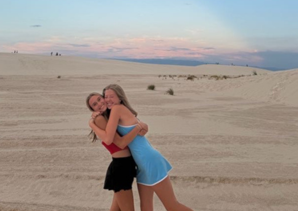 Two young women share a warm hug on the sand dunes.