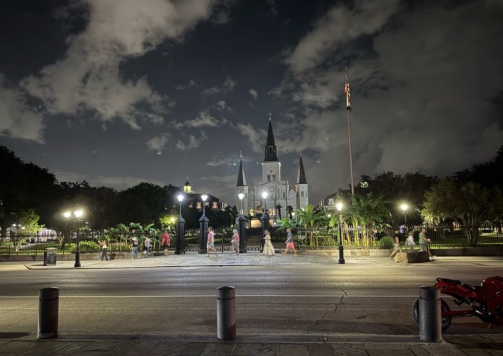 An empty Jackson Square plaza at night, lit by lamplights, with St. Louis Cathedral's spires visible against the night sky.