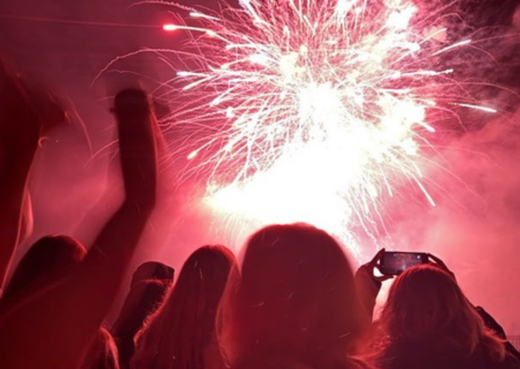red fireworks going off in the background with heads facing away from us