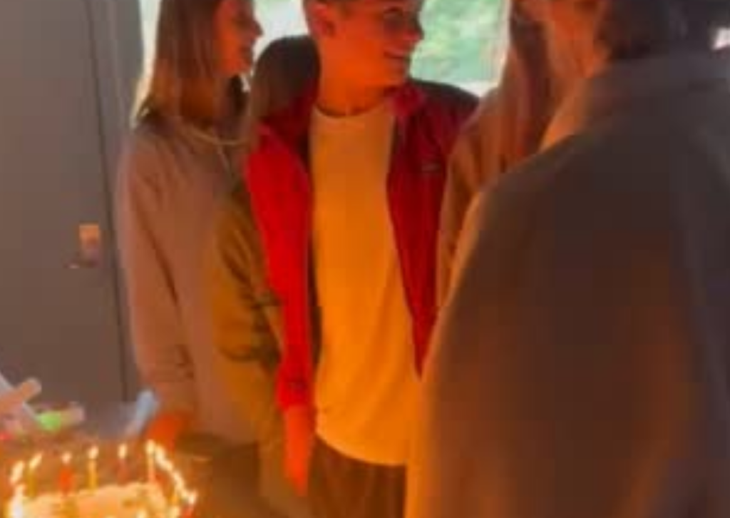 Group of people gathered around a birthday cake with lit candles at a birthday party celebration
