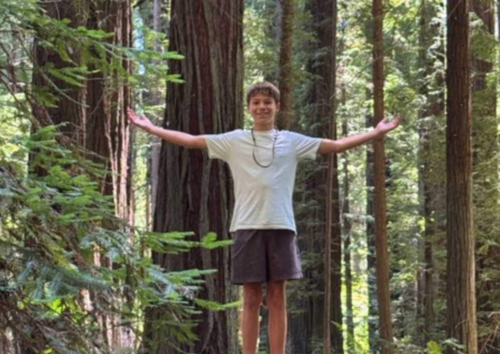 Teenager standing with arms outstretched among tall redwood trees