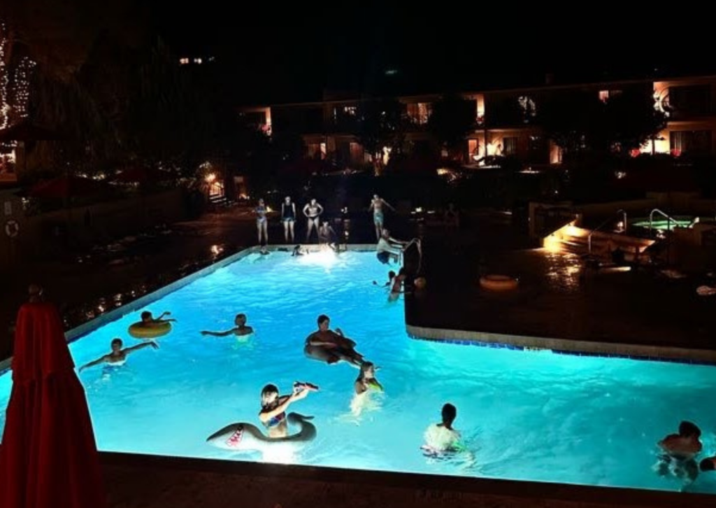 Group swimming and relaxing in a lit outdoor pool at night.