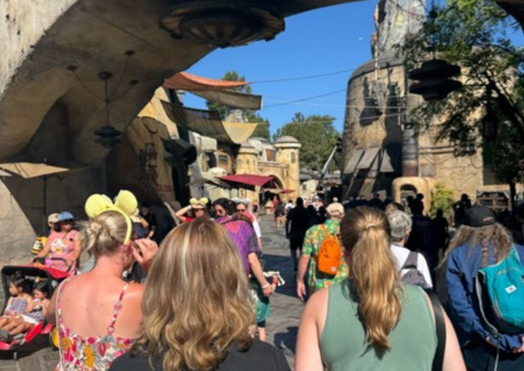Visitors walking through the Star Wars: Galaxy's Edge area of Disneyland, with themed rock formations and buildings in the background.