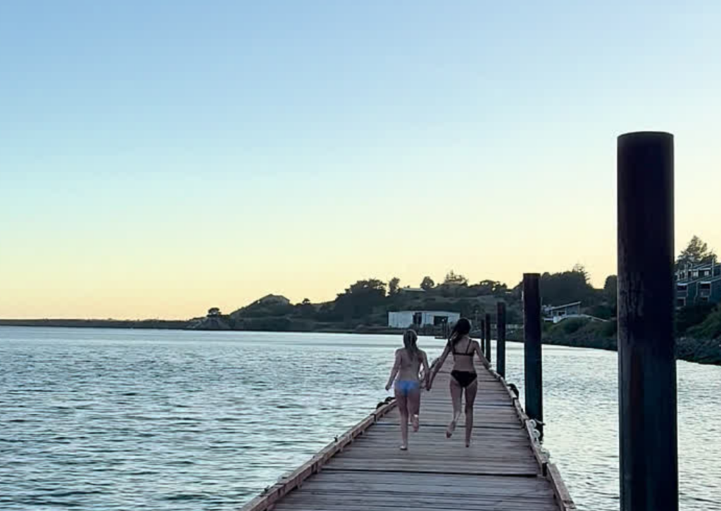 Two women walking hand-in-hand on a wooden dock over the Rogue River at sunset