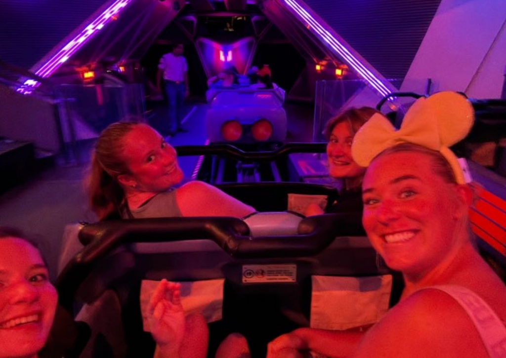 A group of friends smiling for a photo while riding Space Mountain, with neon blue lights glowing around them.