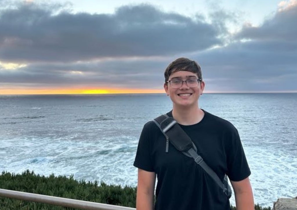 Camper smiling in front of the ocean as the sun sets over the water