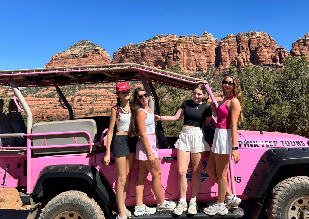 Group posing beside a pink Jeep tour vehicle with red rock formations in the background.
