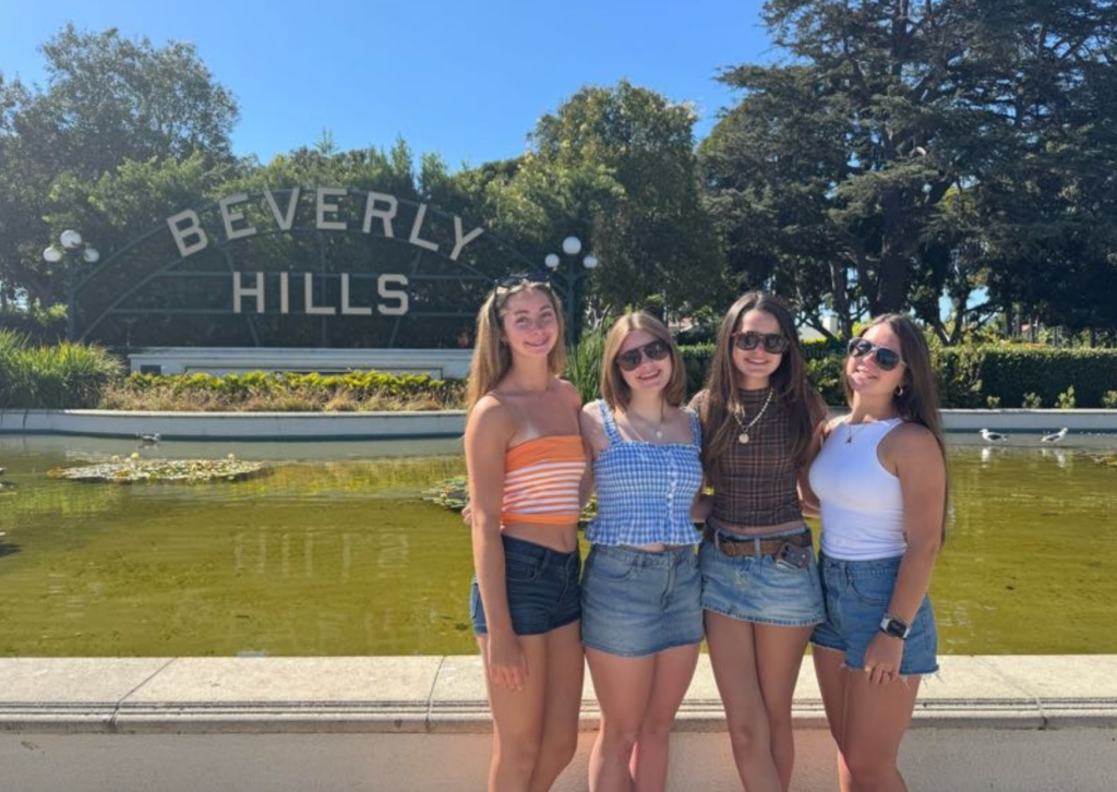 Four women posing in front of the iconic Beverly Hills sign near a fountain in Los Angeles