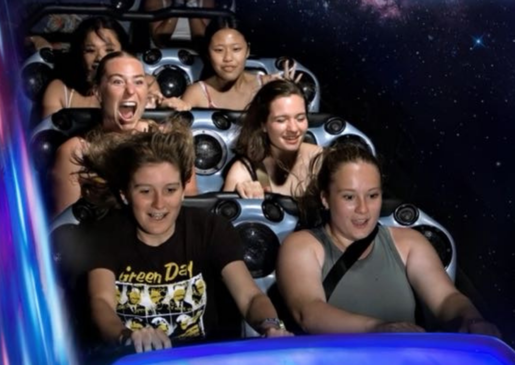 A group of six friends laughing and screaming with excitement on the Space Mountain roller coaster, with a starry background.
