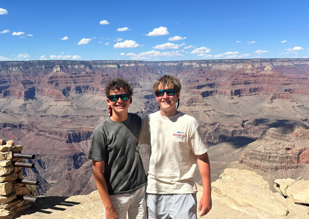 Two friends standing together at a canyon overlook with vast red rock canyon views behind them.
