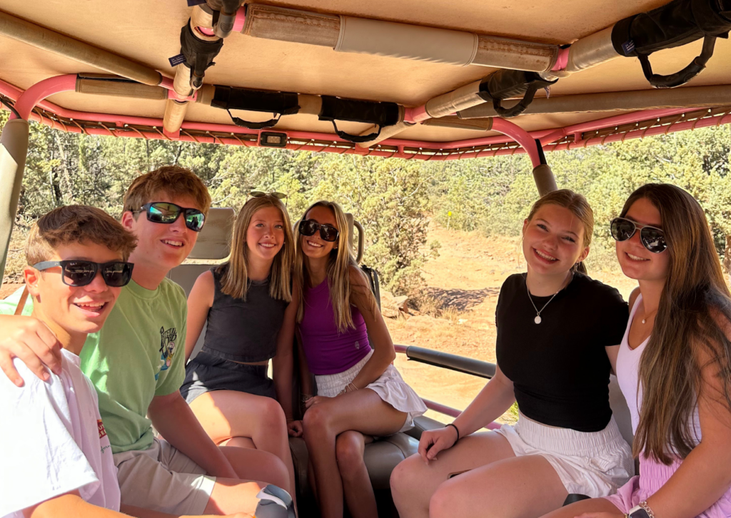 Group of friends smiling and riding together in the open-air back seat of the Pink Jeep tour vehicle.